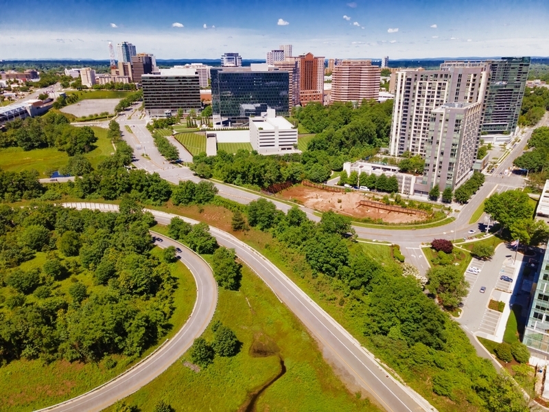 Aerial drone view of curving roads, green fields, and high-rise commercial buildings in Tysons Corner, Virginia.