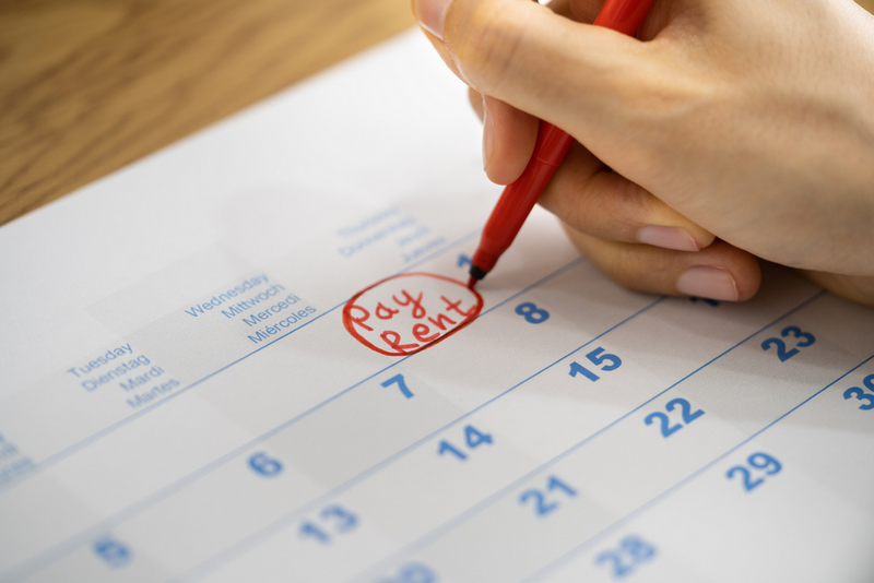 A close-up shot of a person's hand using a red marker to circle the words "Pay Rent" written on a calendar page.