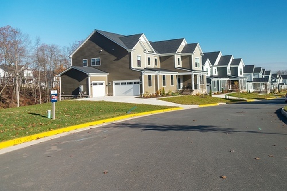A row of modern, multi-story suburban townhouses with dark siding and attached garages along an asphalt street on a clear day.