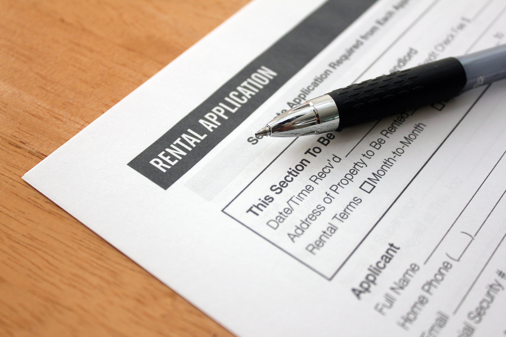 A close-up shot of a white "Rental Application" form with a black pen resting on it, placed on a wooden table.