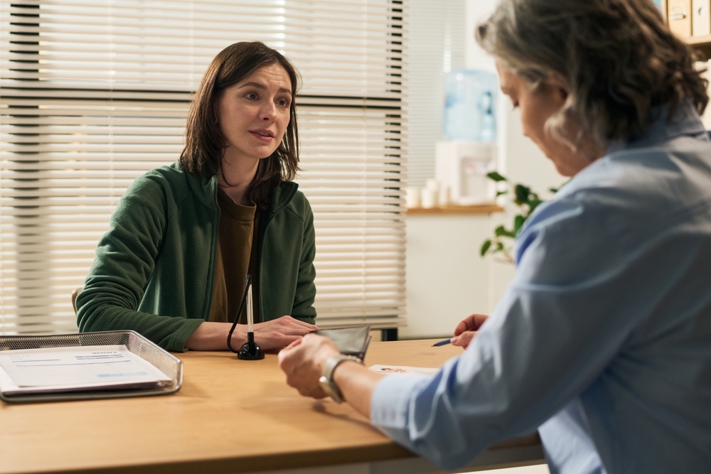 Middle aged Caucasian woman sitting across from middle aged female social worker in office setting