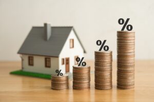 Stack coins as graph trend up and interest rates with house model background