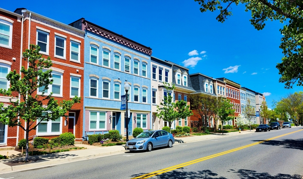 A row of colorful multi-story row houses lined up along a city street under a bright blue sky.