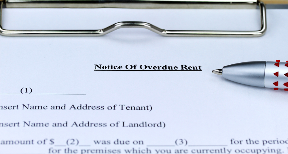 An overdue rent form on a metal clipboard with a ball point pen