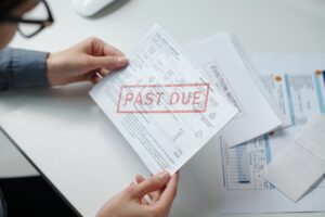 High angle closeup of female hand holding late bills while sorting financial documents over table copy space