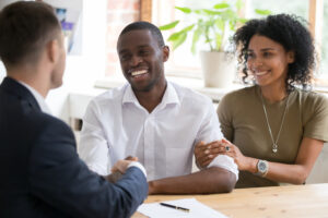 Happy black couple first time home owners handshaking realtor insurer