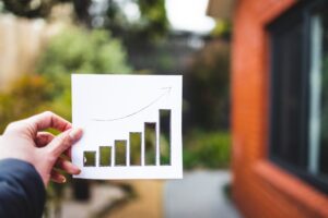 hand holding real estate graph showing stats going up with cut outs in front of house exterior and backyard