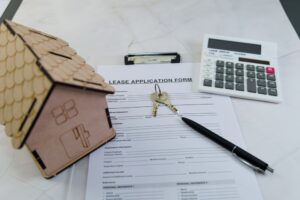 A lease application form is filled out alongside a wooden house model, keys, and a calculator.
