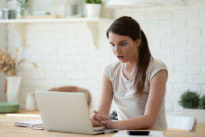 young woman using calculator and laptop for calculating finance rates looking at screen